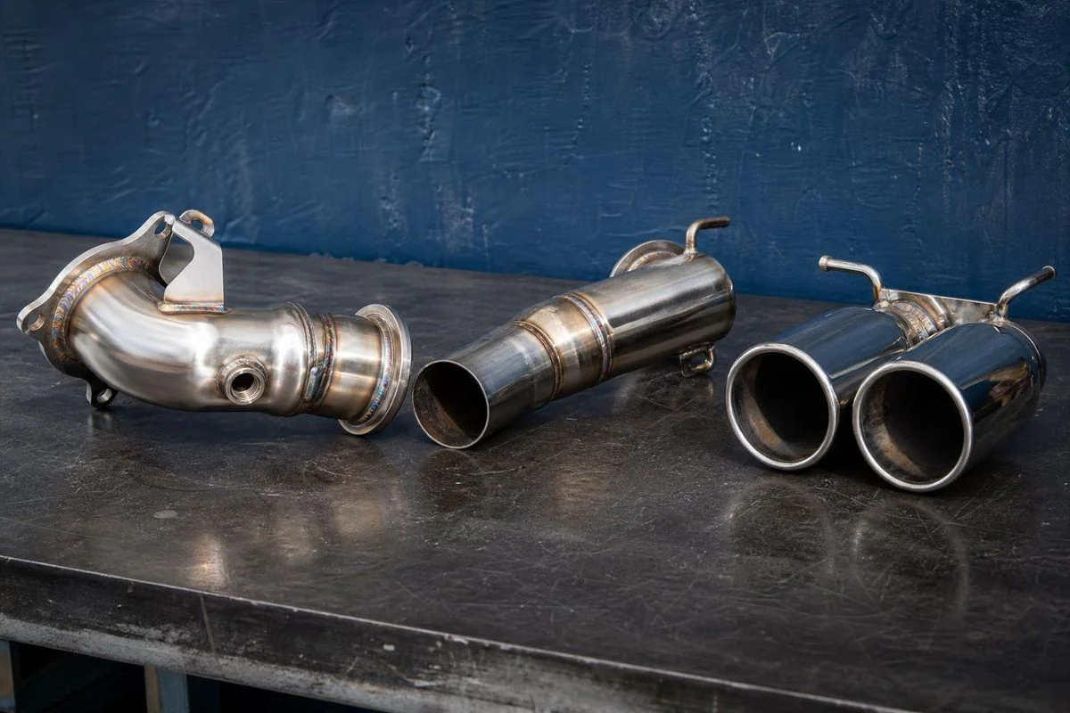 Sistema de escapamento em aço inox polido sobre a bancada, com downpipe, tubo central e ponteiras